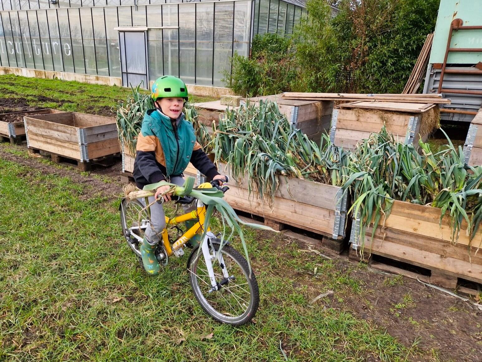 Kind op fiets met prei in zelfoogsboerderij